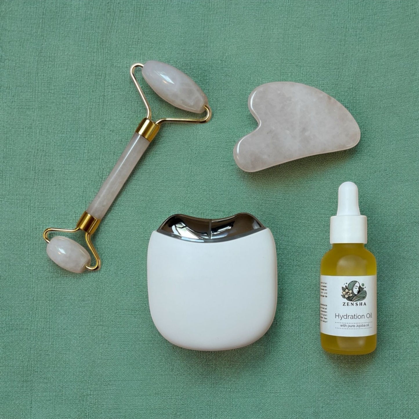 A Zensha Face oil laying next to a EMS Gua Sha Product and a Gua Sha Stone on a green background