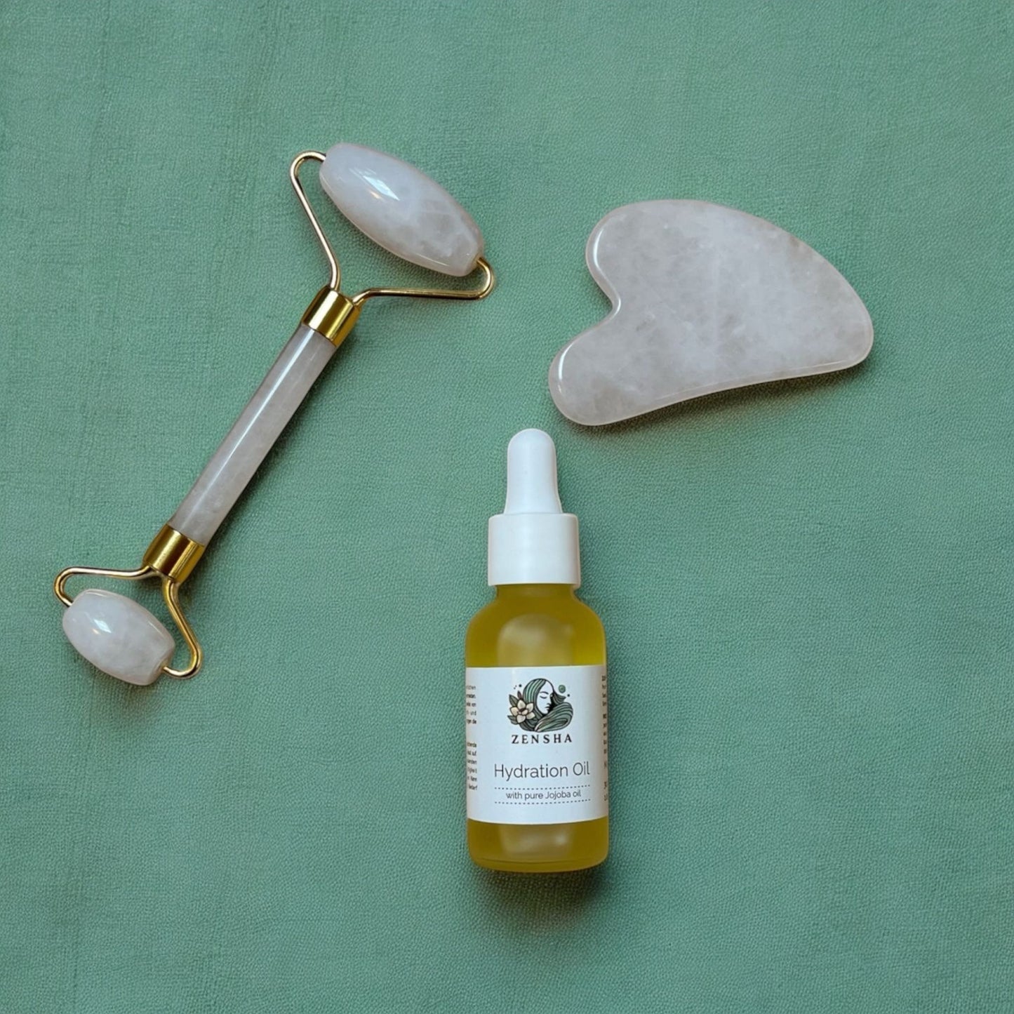 A Set of a Gua Sha Stone, Jade Roller and hydration oil laying next to each other on a green background